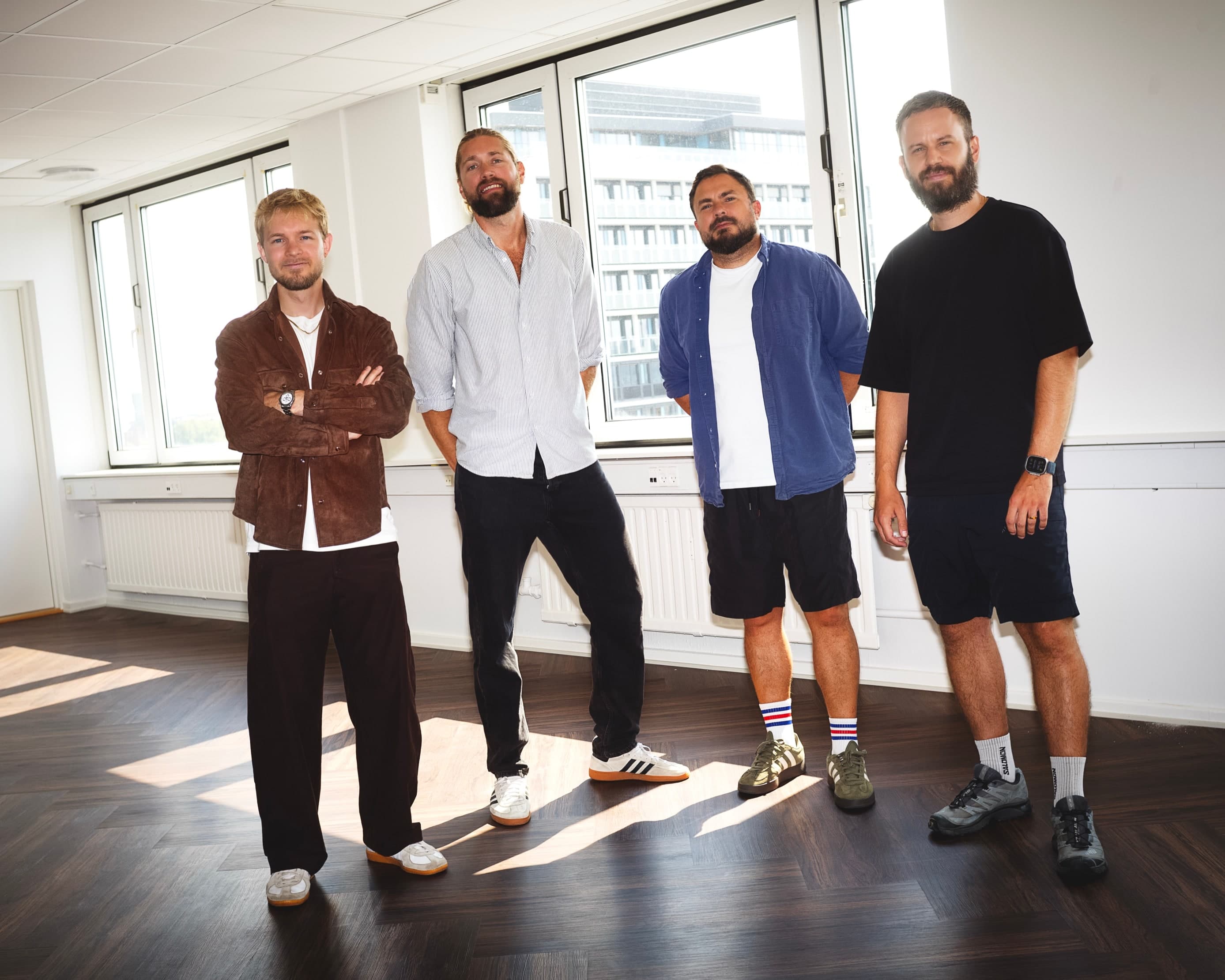 The four Palette founders standing together in the company's Copenhagen office, with the city visible through the windows behind them.